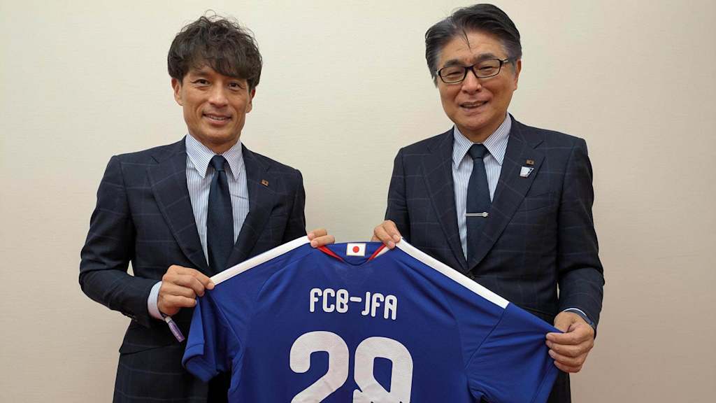 JFA-Präsident, Mr. Miyamoto Tsuneyasu (links) und der Technical Director, JFA Technical Committee, Mr. Yamamoto Masakuni (rechts) halten ein blaues Trikot hoch.