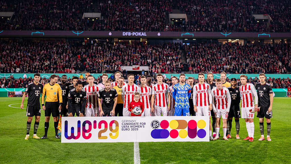 Spieler des FC Bayern und des 1. FC Köln stehen gemeinsam vor einem Banner für die Bewerbung des DFB für die Frauen-EM 2029