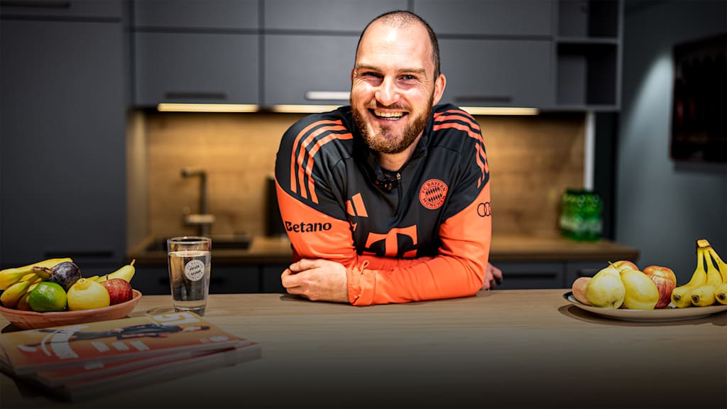 Melf Carstensen lehnt in der FC Bayern Teamline lachend über einen Tisch.