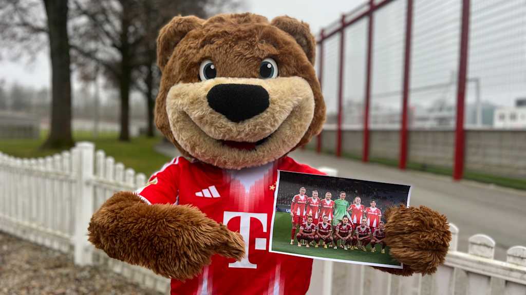 Berni sitzt draußen auf einem Stuhl und zeigt auf das Fehlersuchbild der FC Bayern Frauen Mannschaft.
