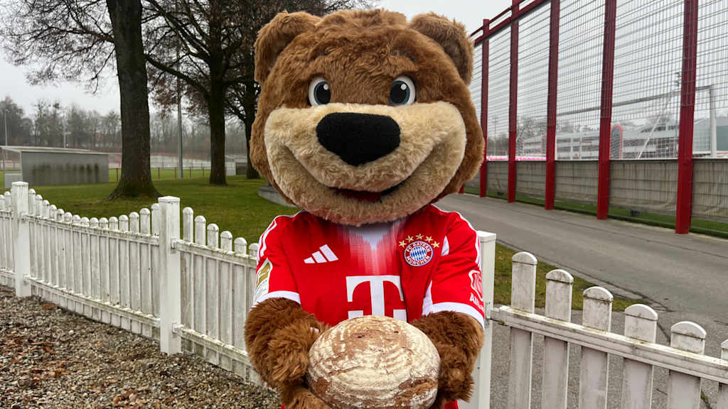 Berni sitzt draußen auf einem Stuhl und hält ein Laib Brot in seinen Tatzen.