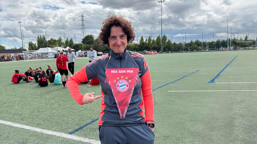 Ivon Karras deutet auf einen "Mia-San-Mia"-Wimpel.