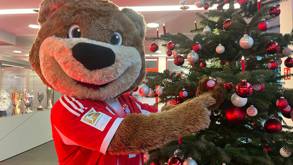 Berni steht vor einem geschmückten Weihnachtsbaum und zeigt auf eine FC Bayern Kugel.