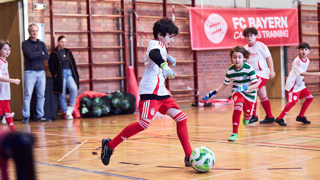 Ein Kind im FC Bayern Trikot dribbelt in einer Halle.