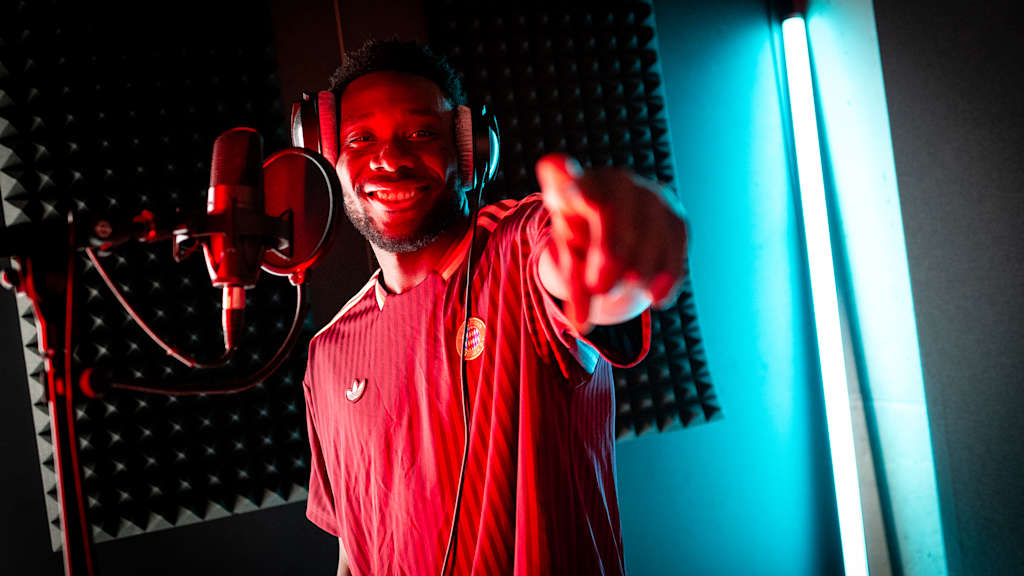 Alphonso Davies steht vor einem Mikro und zeigt in die Kamera