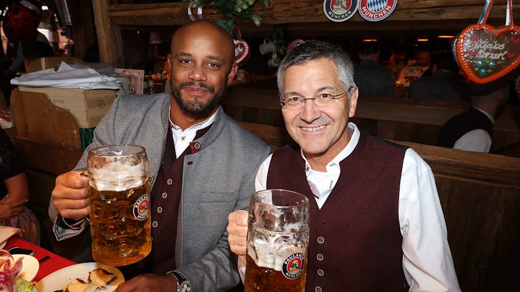 Herbert Hainer and Vincent Kompany smile and hold up a beer in at the Oktoberfest.