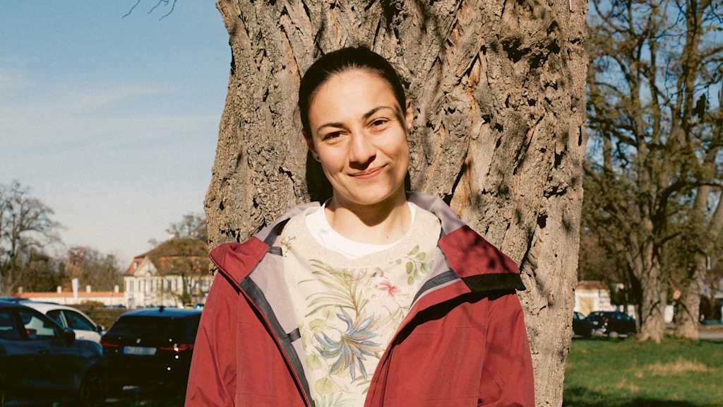 Mala Grohs steht vor einem Baum und lächelt.