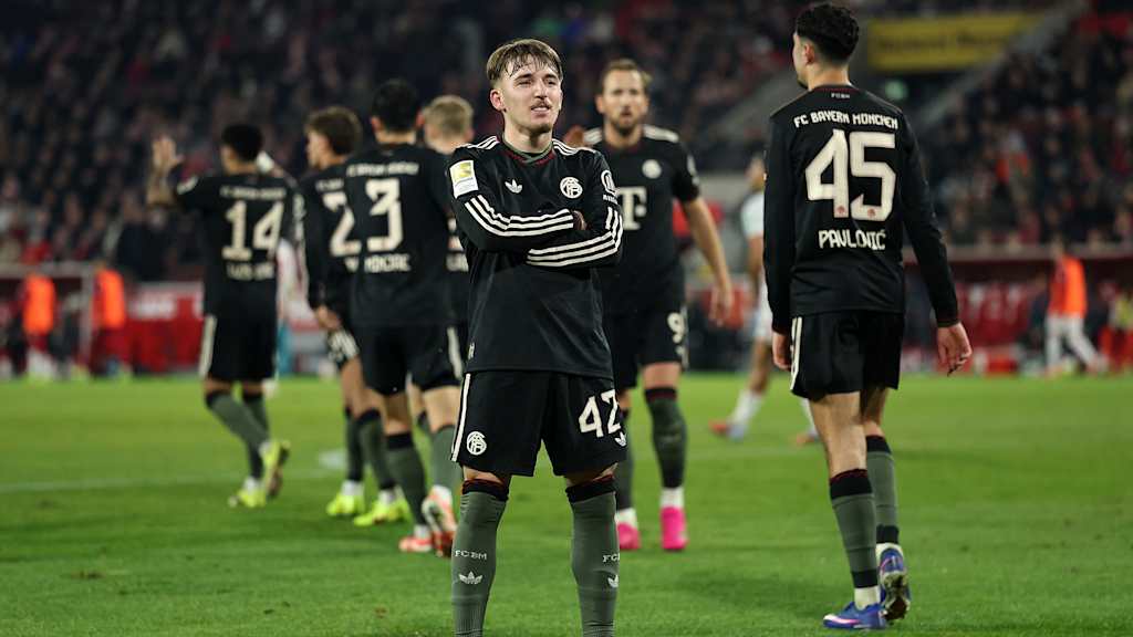 Lennart Karl steht mit verschränkten Armen vor der Kurve nach dem 3:1 im Bundesliga-Spiel des FC Bayern beim 1. FC Köln