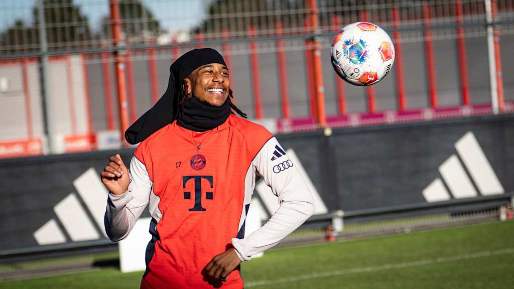 Michael Olise schaut einen Ball an und lacht im Training des FC Bayern