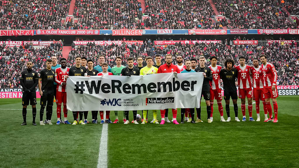 Die Mannschaften des FC Bayern und des FC Augsburg halten vor Anpfiff der Partie ein Banner mit der Aufschrift: #WeRemember