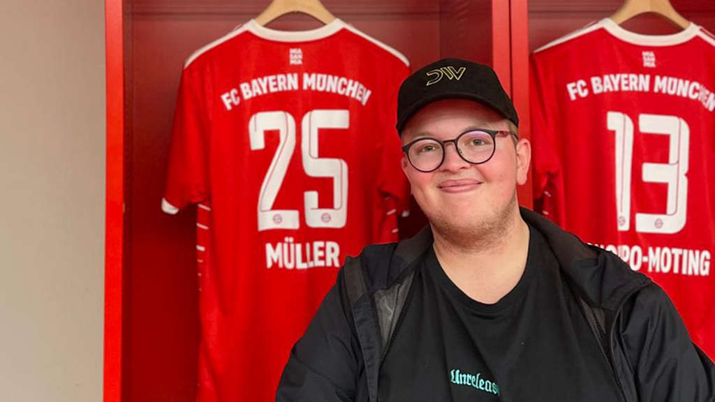 FC Bayern-Fan Glenn sitzt in der Kabine der Allianz Arena vor einem Trikot von Thomas Müller