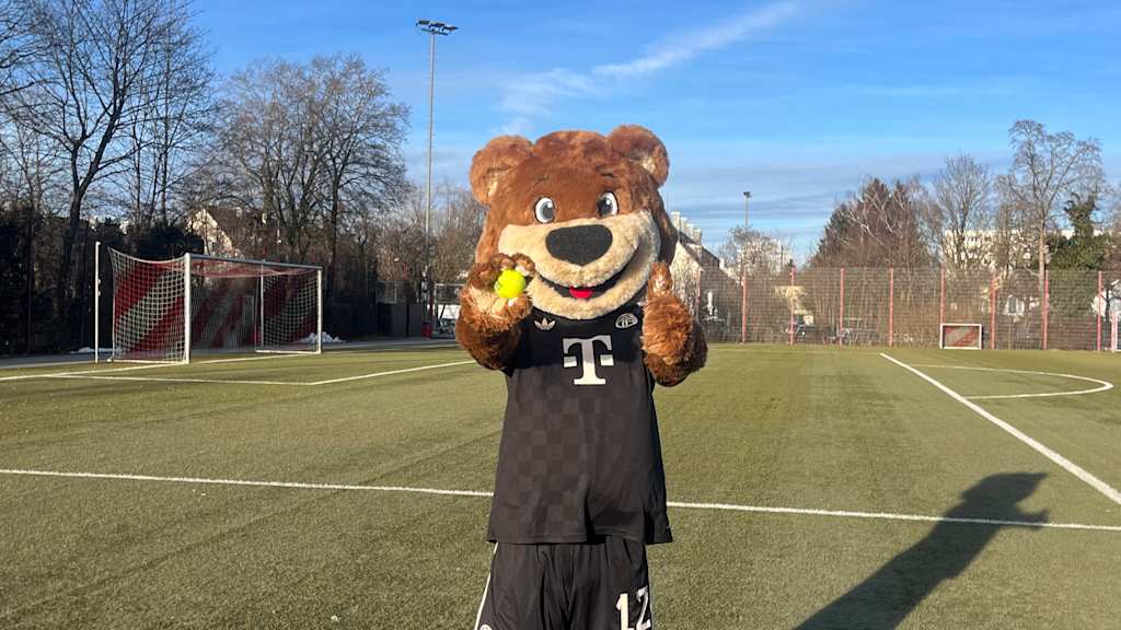 Berni auf dem Kunstrasenplatz mit einem Tennisball in der Hand und Daumen hoch.