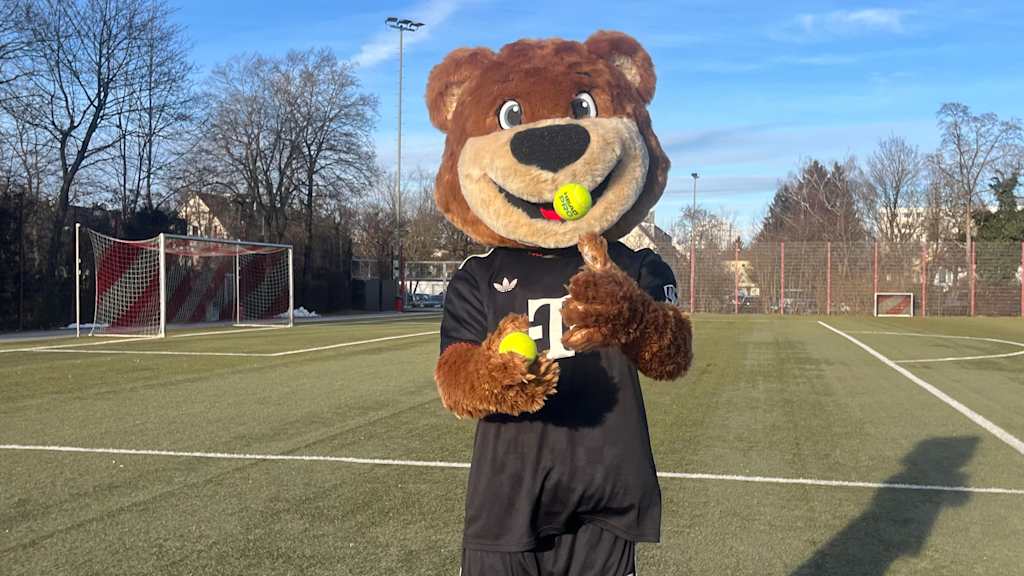 Berni auf dem Kunstrasenplatz und wirft einen Tennisball hoch.