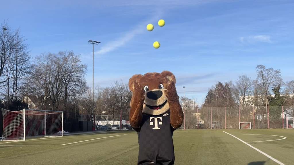 Berni auf dem Kunstrasenplatz und wirft drei Tennisbälle hoch.