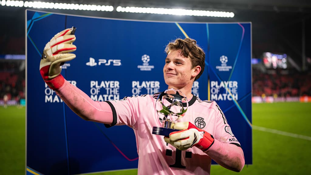 Jonas Urbig in Pink macht einen Selfie mit der Man of the Match Trophäe.