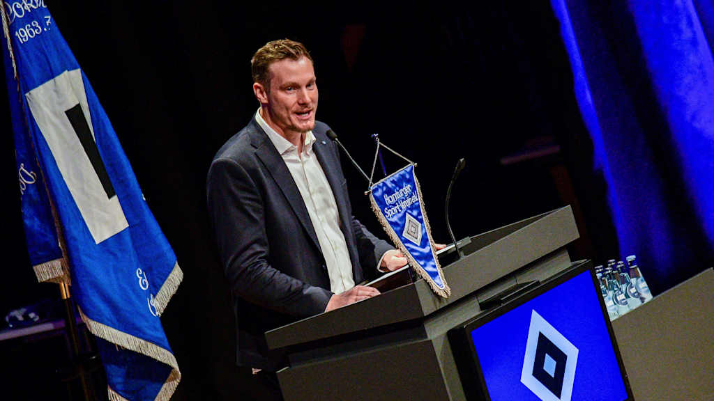 Jansen steht im Anzug an einem Redner-Pult.