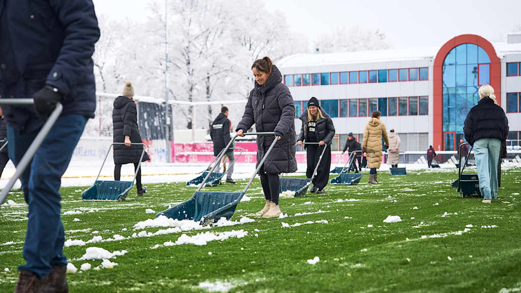 Mitarbeiterinnen und Mitarbeiter des FC Bayern beim Schneeschieben an der Säbener Straße