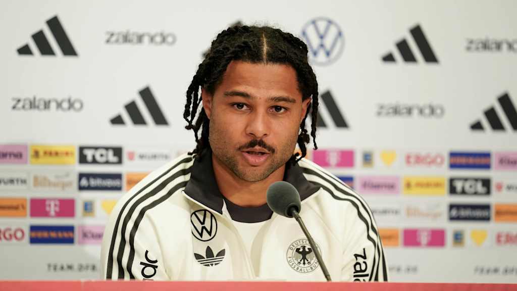 Serge Gnabry im weißen Dress auf der Pressekonferenz.
