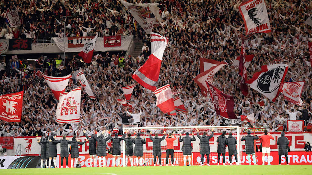 Spieler des SC Freiburg hüpfen Arm in Arm vor der Fankurve