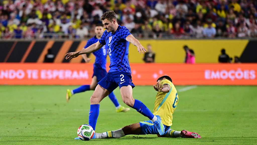Josip Stanisic spielt einen Pass gegen einen grätschenden brasilianischen Spieler