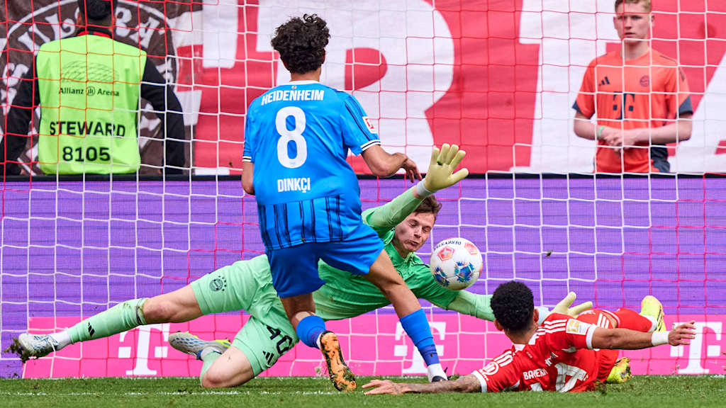 Jonas Urbig pariert gegen Eren Dinkci im Bundesliga-Spiel des FC Bayern gegen den 1. FC Heidenheim einen direkten Freistoß zum 1:2 im Bundesliga-Spiel des FC Bayern gegen den 1. FC Heidenheim
