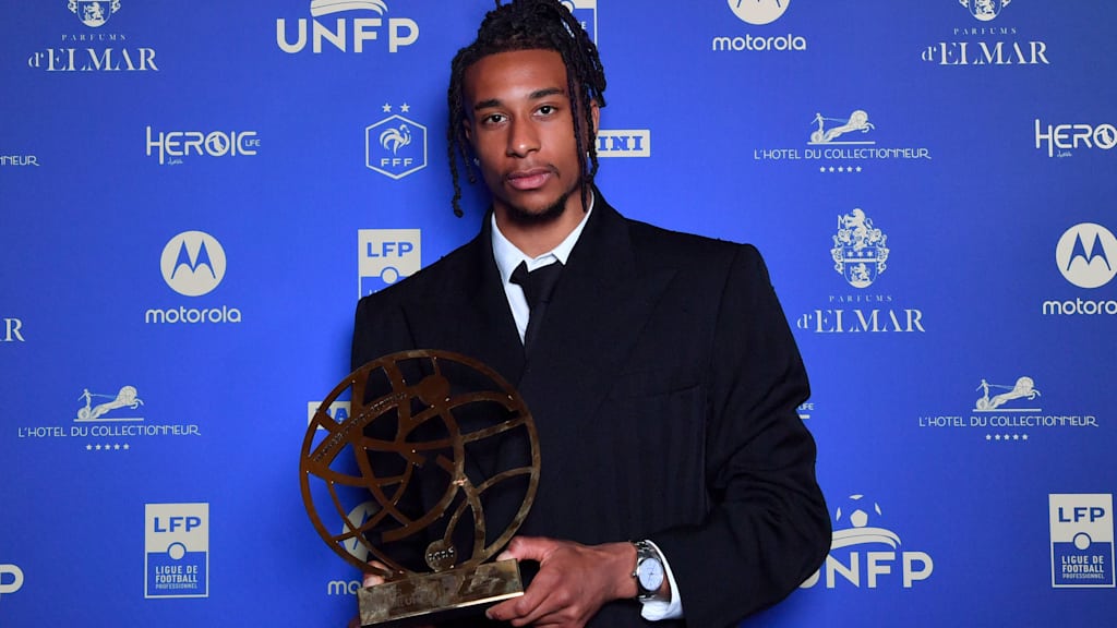 Michael Olise looks into the camera holding a trophy in front of a blue background