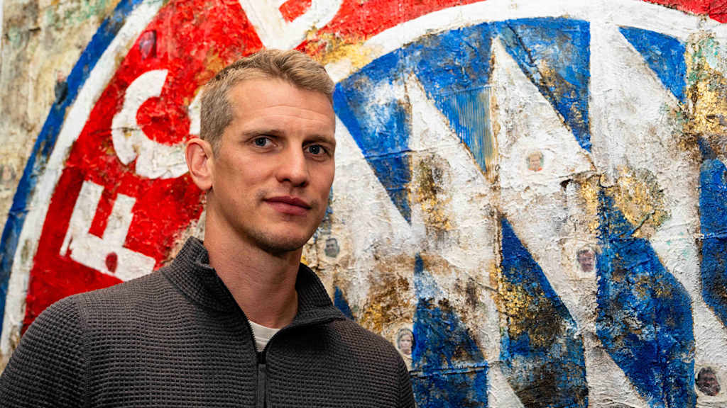 Lars Bender steht vor dem FC Bayern Logo und schaut in die Kamera.