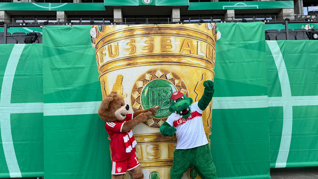 Berni mit dem Maskottchen des VfB Stuttgarts vor einem Poster des DFB.-Pokals.