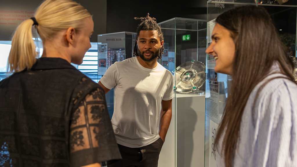 Serge Gnabry, Pernille Harder and Jovana Damnjanovic chat in front of the trophies at the FC Bayern Museum