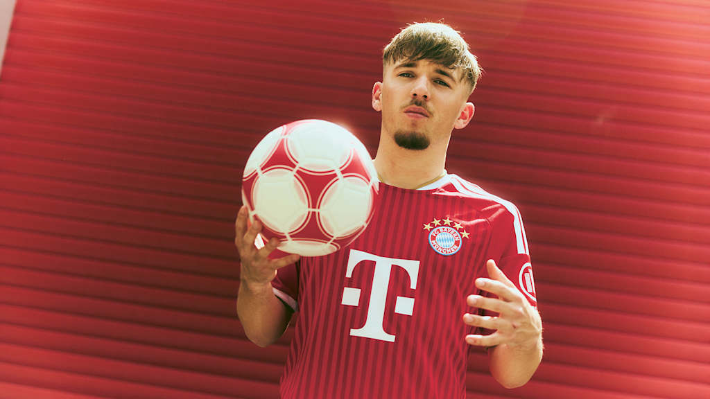 Lennart Karl steht im FC Bayern Trikot vor einem roten Tor und hält einen Ball in der Hand