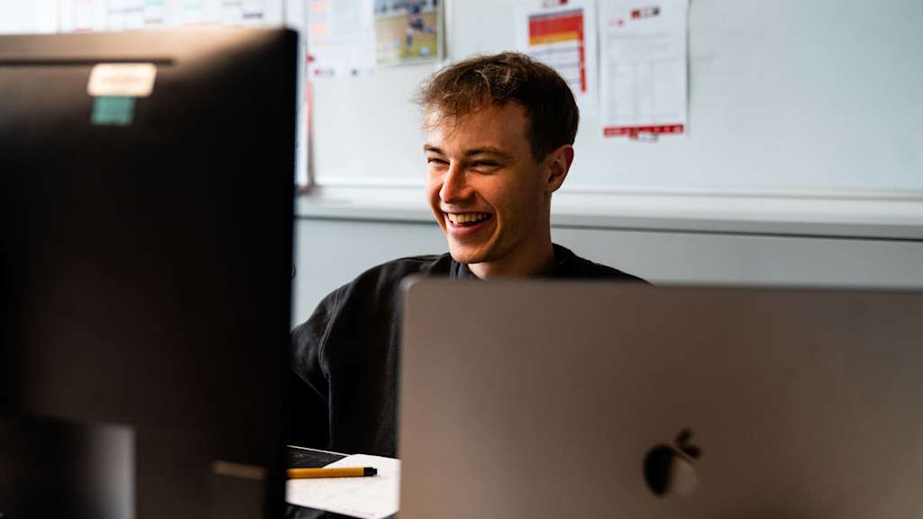 Moritz Mosandl sitzt lachend am Schreibtisch in einem Büro am FC Bayern Campus