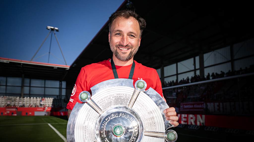 Trainer José Barcala hält die Meisterschale in den Händen und lächelt.