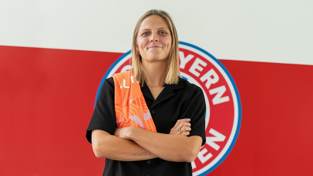 Anna Wellmann steht vor einer Wand mit FC Bayern Logo und hat ihr Trikot über der Schulter.