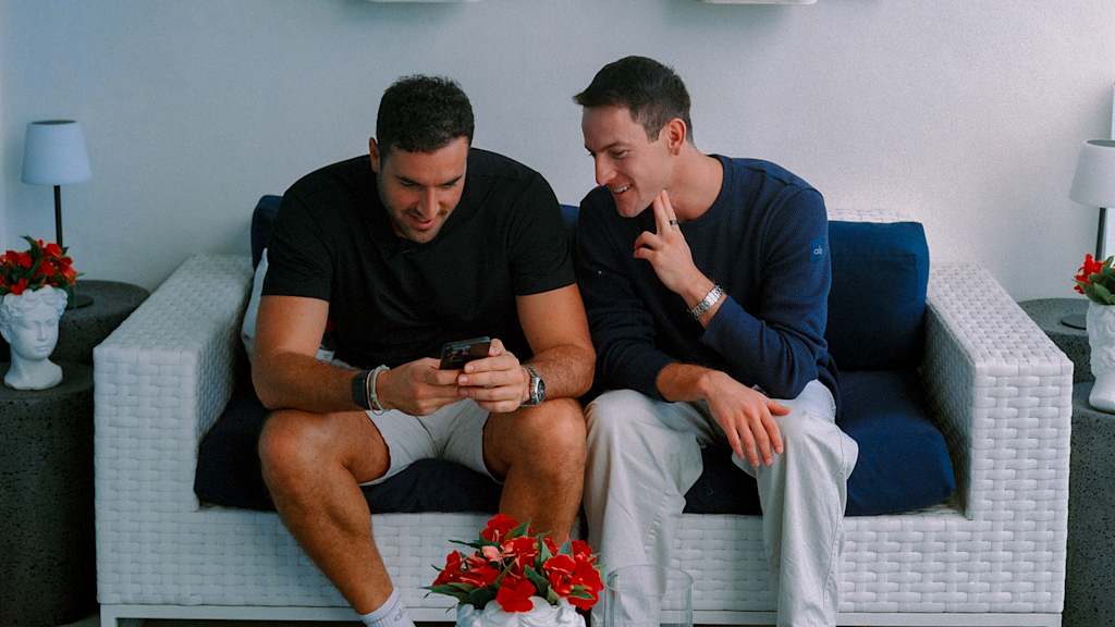 Zwei Männer sitzen auf einer Couch und schauen auf ein Handy