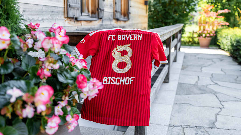 EIn rotes FC Bayern Trikot mit dem Sonderflock für das Hongkong-Spiel von Tom Bischof hängt auf einem Tisch