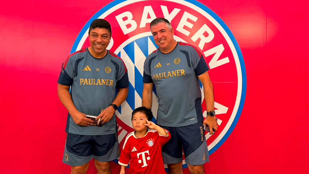 Giovane Elber und Roy Makaay machen ein Foto mit einem Kind vor einem FC Bayern-Logo