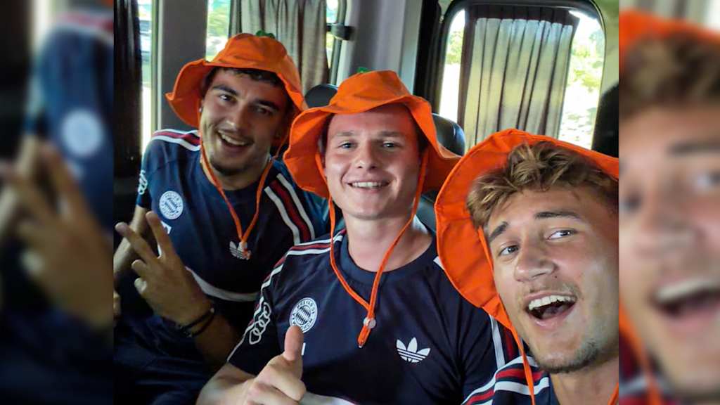 Aleksandar Pavlovic, Jonas Urbig und Tom Bischof tragen orangefarbene Sonnenhüte und posieren für ein Foto