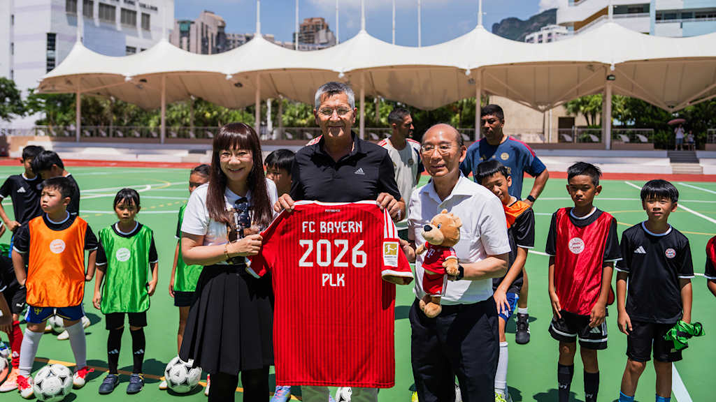 Herbert Hainer and two organisers of the kids training session hold up an FC Bayern shirt