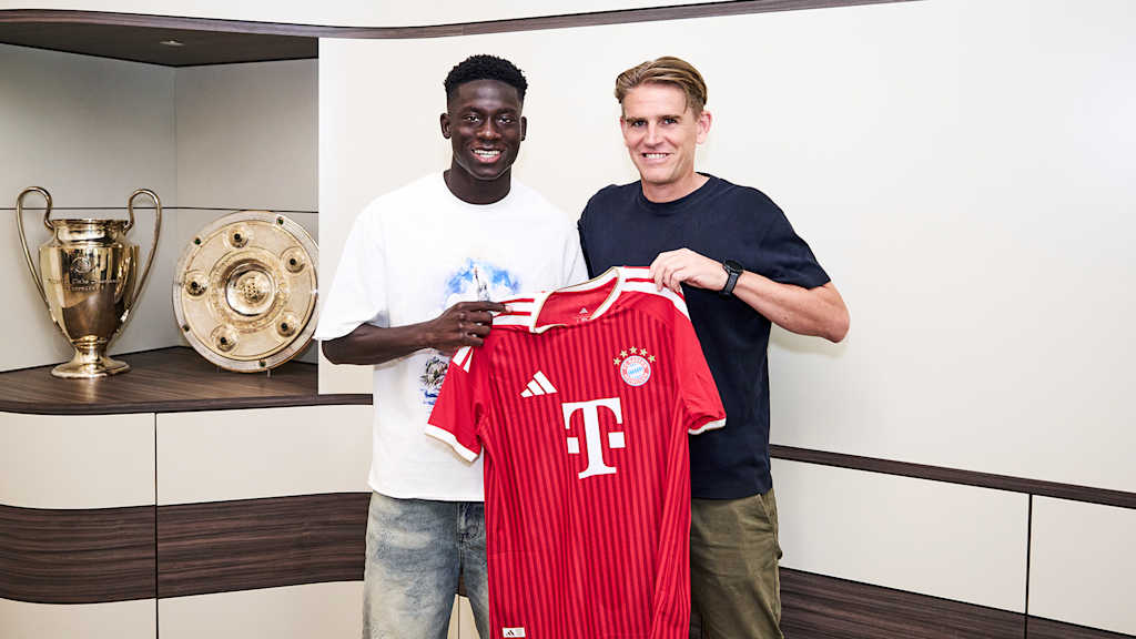Bara Ndiaye und Christoph Freund halten ein rotes FC Bayern Trikot