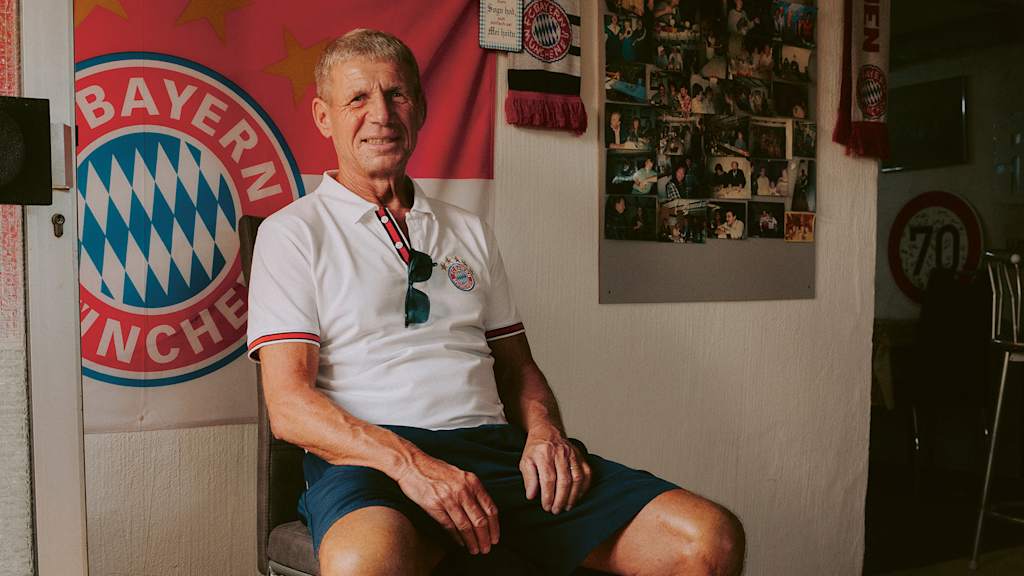Ex-Bundesliga striker Klaus Müller sits on a chair in front of an FC Bayern flag