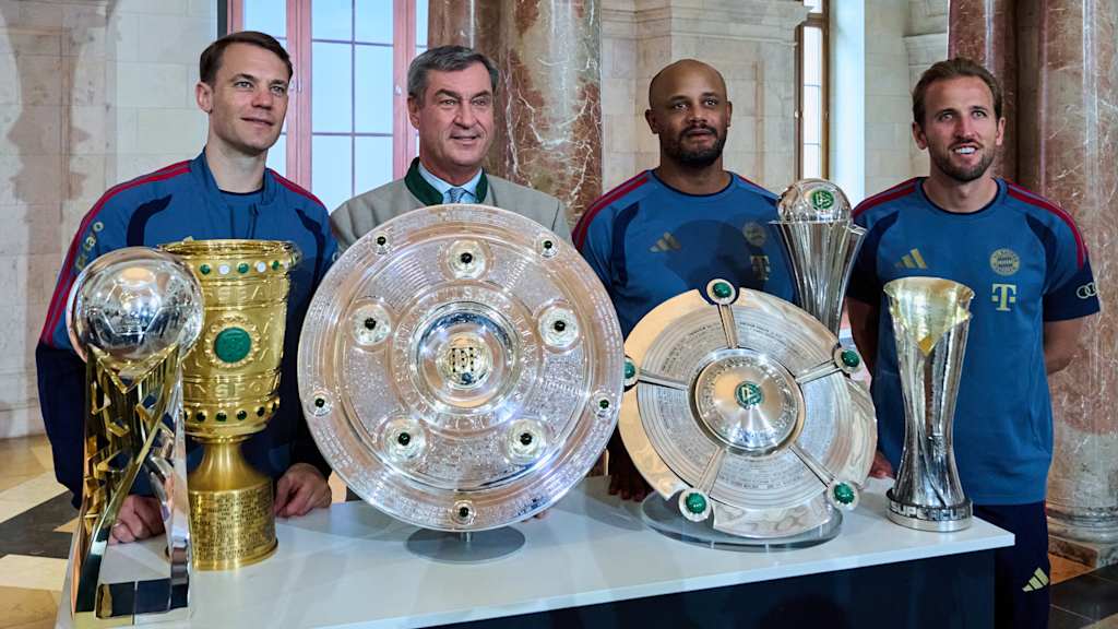 Kapitän Manuel Neuer, Ministerpräsident Markus Söder, Cheftrainer Vincent Kompany und Torjäger Harry Kane posieren vor den Trophäen