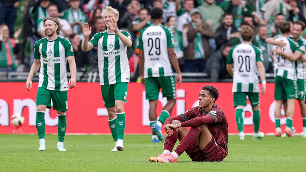 Augsburg's Noahkai Banks sits disappointed on the floor while Bremen players celebrate