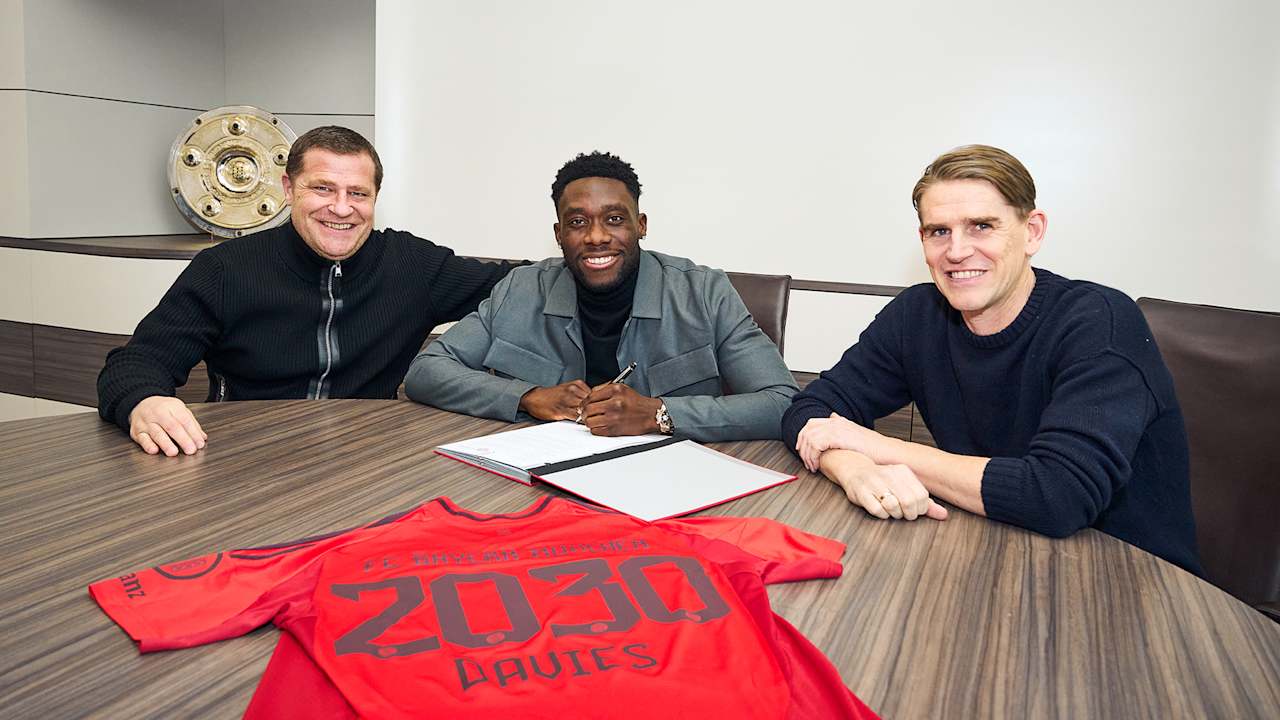 Max Eberl, Alphonso Davies und Christoph Freund sitzen an einem Tisch, Davies unterschreibt einen Vertrag