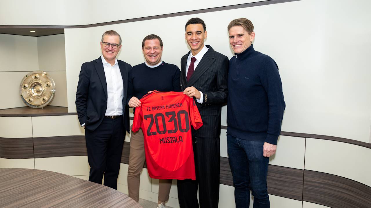 Jan-Christian Dreesen, Max Eberl, Jamal Musiala und Christoph Freund stehen nebeneinader und halten ein Bayern-Trikot hoch mit 2030 Musiala