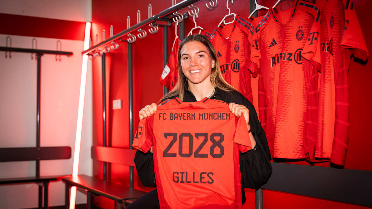 Vanessa Gilles hält lächelnd das FC Bayern Trikot mit ihrem Namen und der Vertragslaufzeit 2028 in die Kamera.
