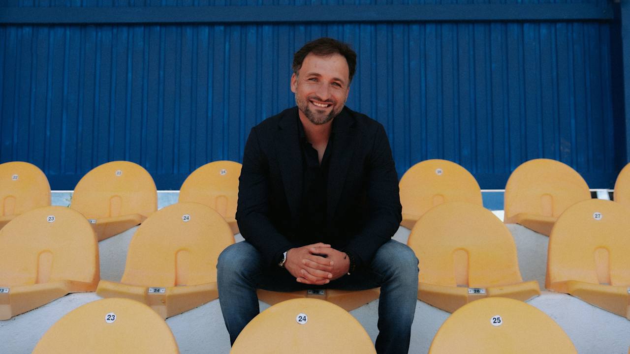 Trainer der FC Bayern Frauen José Barcala sitzt auf einer Tribüne und lächelt in die Kamera