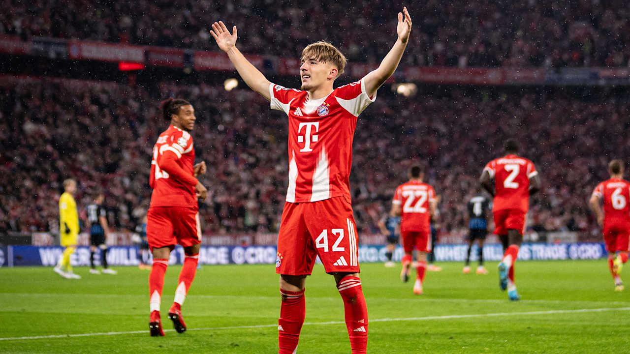 Nach seinem 1. Champions League-Tor für den FC Bayern gegen Club Brügge steht Lennart Karl mit ausgebreiteten Armen vor der Fankurve.