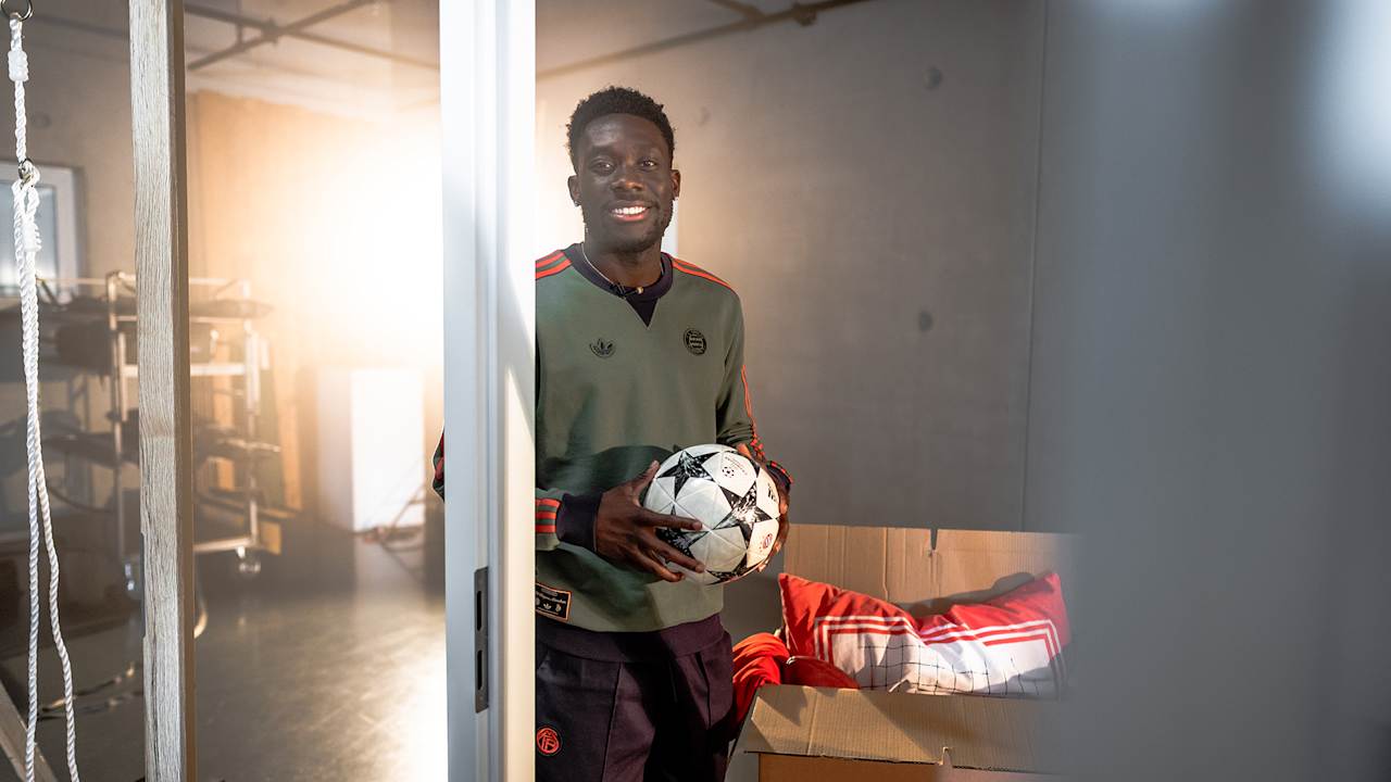 Alphonso Davies steht mit einem Ball in der Hand in einer Tür