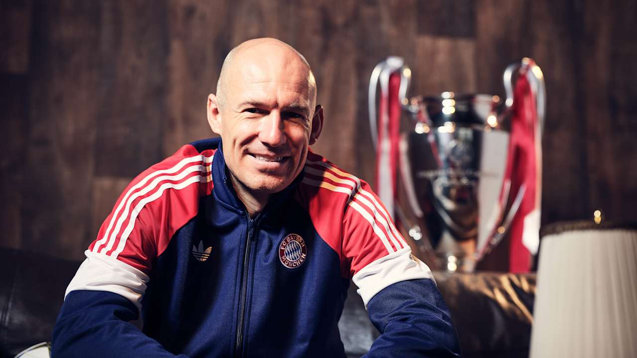 A grinning Arjen Robben in an FC Bayern training jacket on a couch.