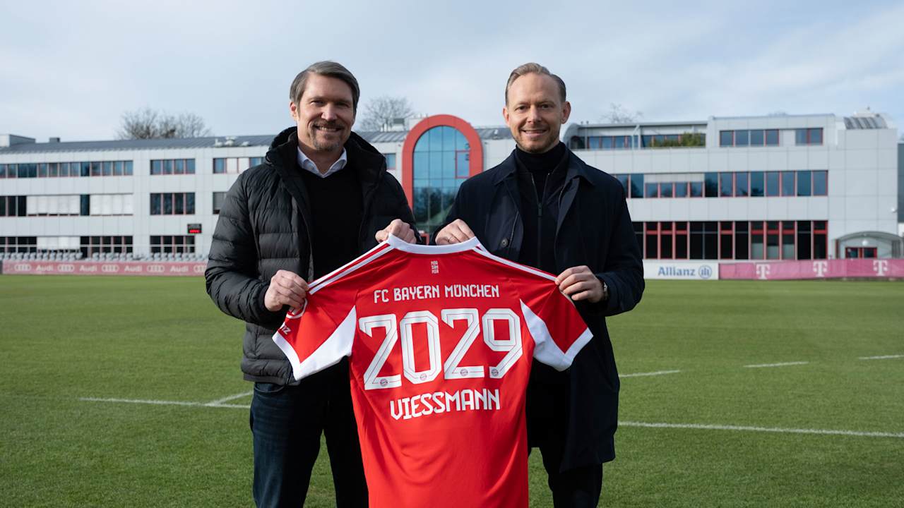 Rouven Kasper, Vorstand Marketing und Vertrieb FC Bayern, und Thomas Heim, President Climate Solutions Europe bei Carrier, halten an der Säbener Straße ein FC Bayern-Trikot mit dem Schriftzug 2029 Viessmann